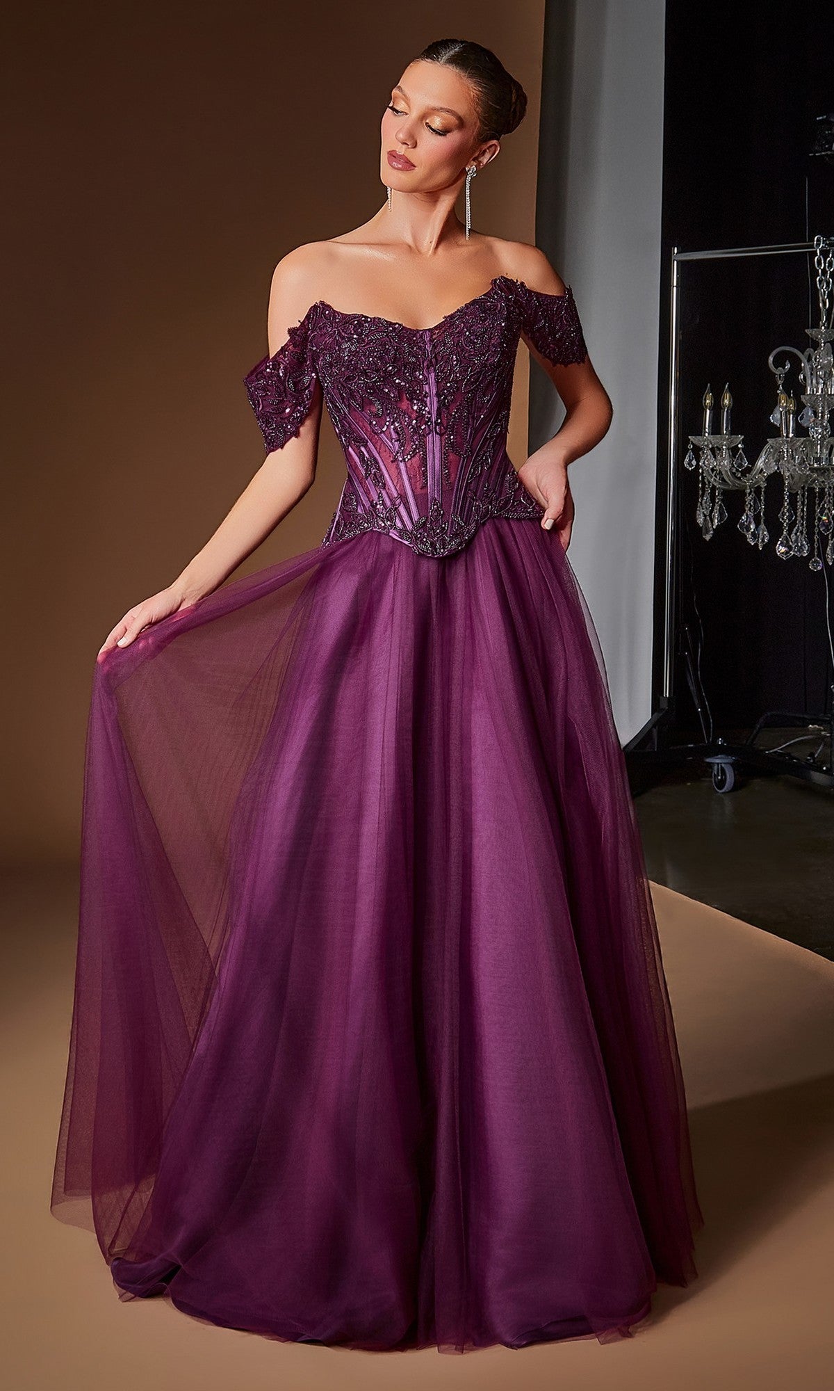 A woman stands against a brown background wearing the Ladivine CD657 Long Prom Dress in eggplant—an off-the-shoulder, floor-length ball gown featuring a corset bodice and flowing tulle skirt.